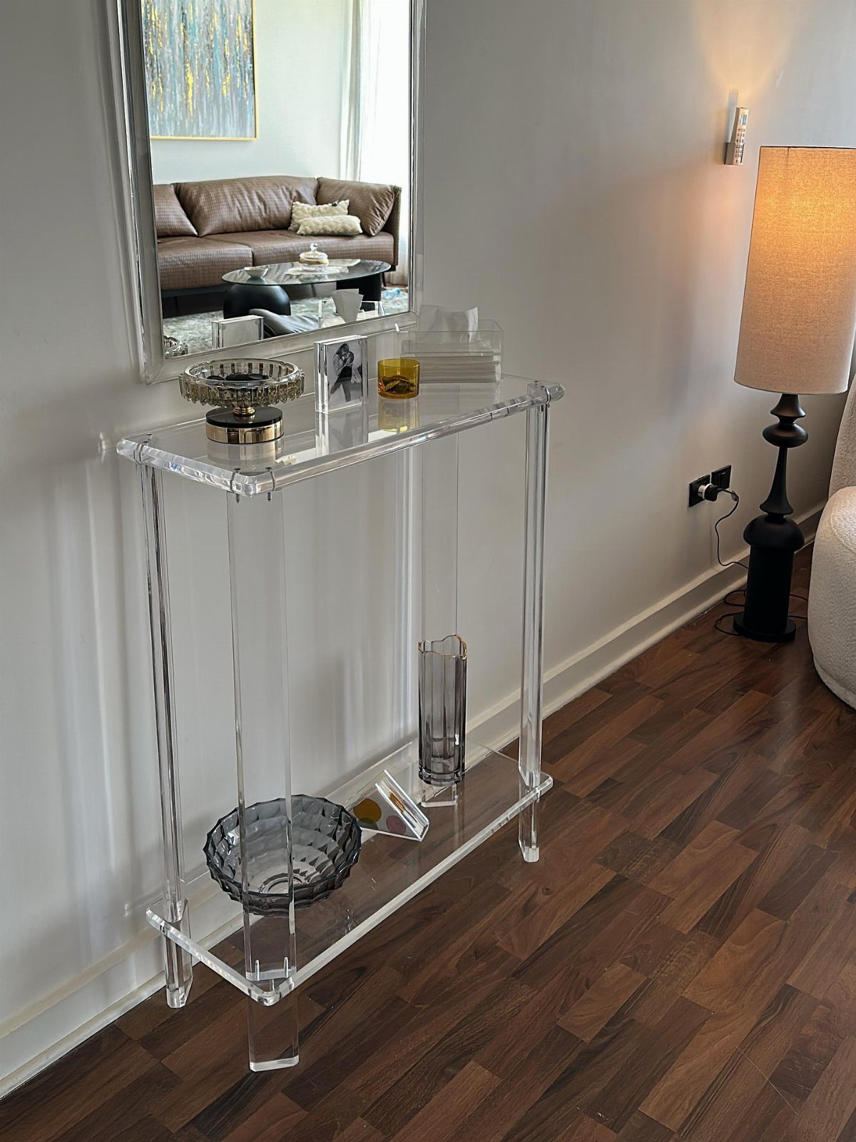 Clear acrylic console table against a grey wall with a mirror above it.