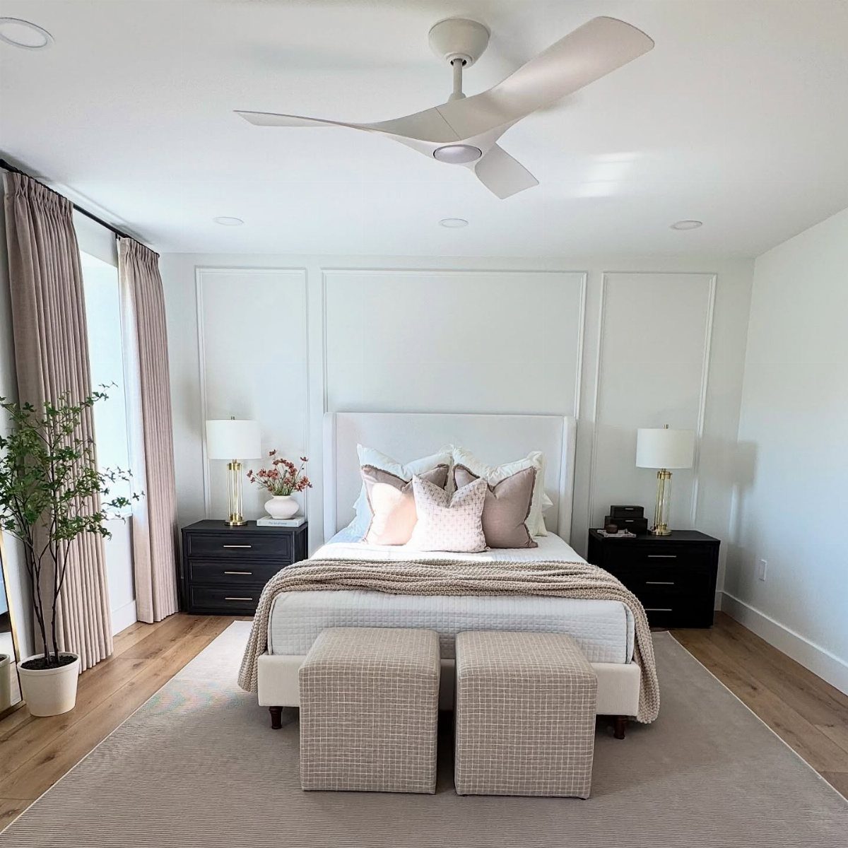 Modern white bedroom with a three-blade ceiling fan and neutral toned bedding.