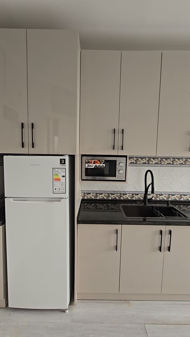 Small beige kitchen units with a black countertop, sink, and white refrigerator.