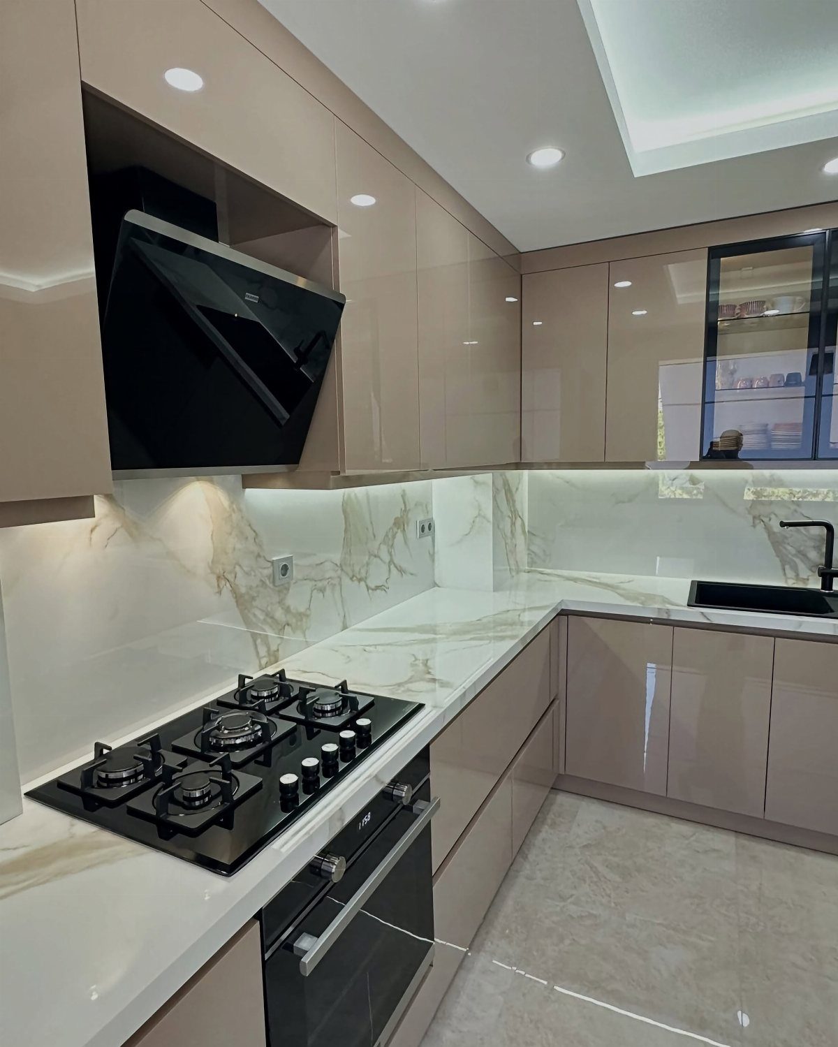 Glossy beige kitchen cabinets with white marble countertops and black appliances.