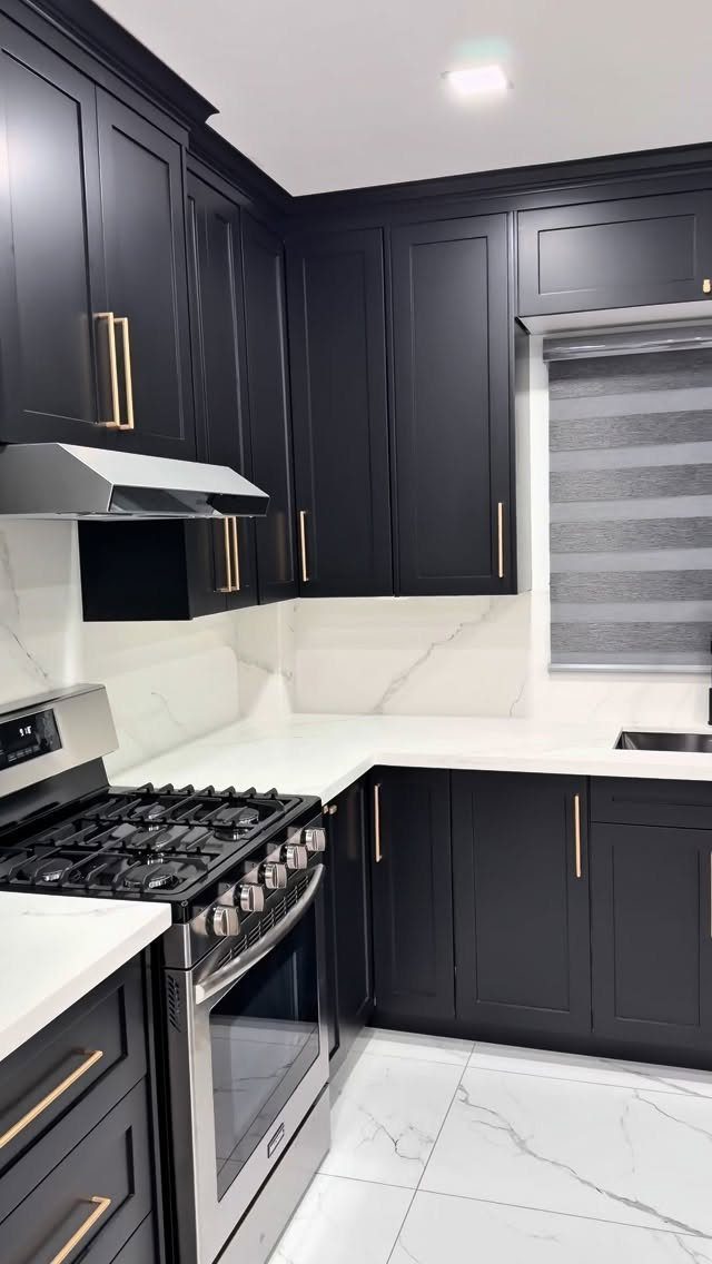 Dark black kitchen cabinets with gold hardware and white marble countertops.