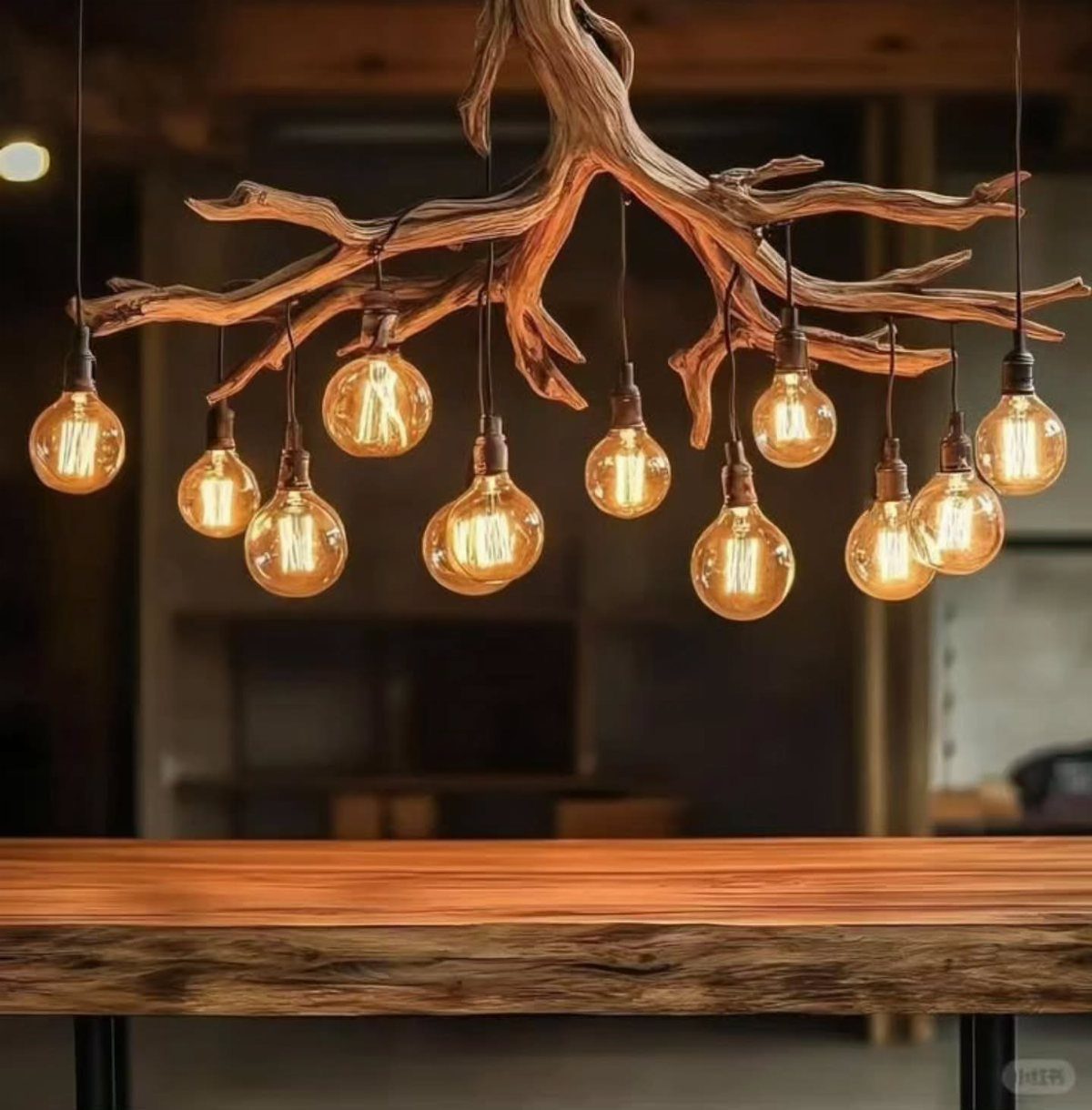 Rustic wooden branch chandelier with glowing Edison bulbs hanging over a wooden table.