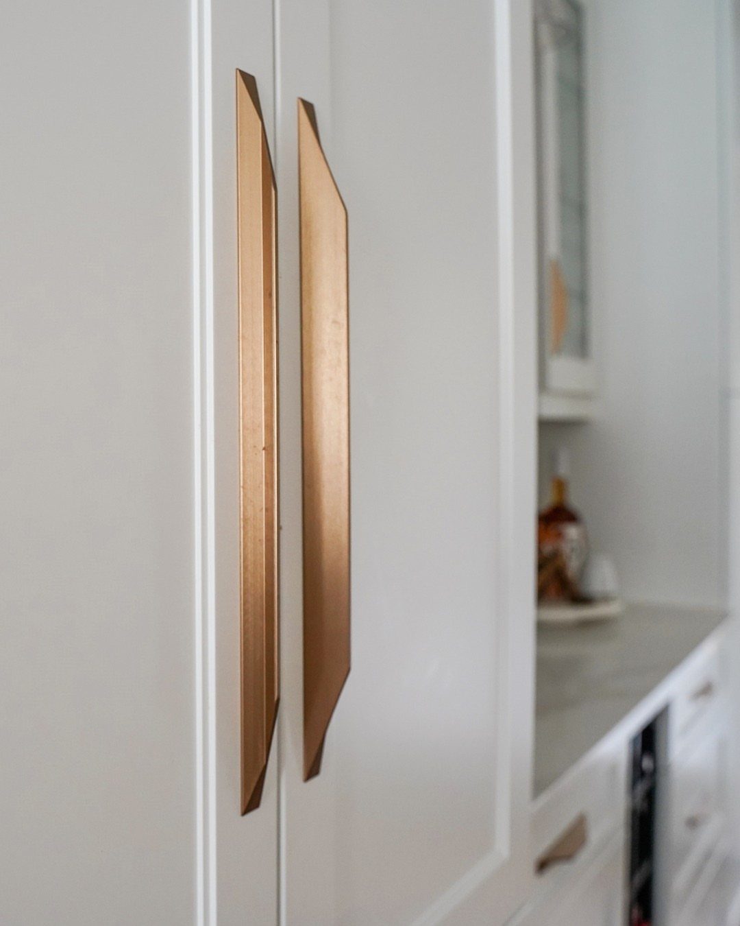 Brushed gold cabinet handles on white shaker doors in a bright kitchen.