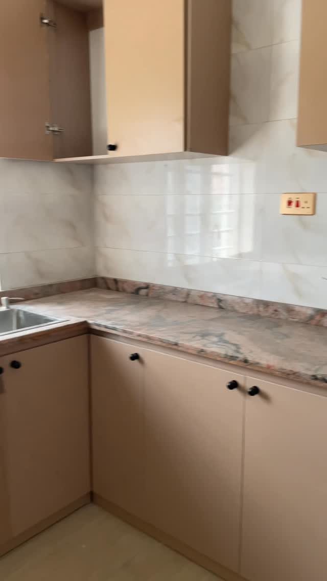 Beige built-in kitchen cabinets with a marbled granite countertop and white tiled backsplash.