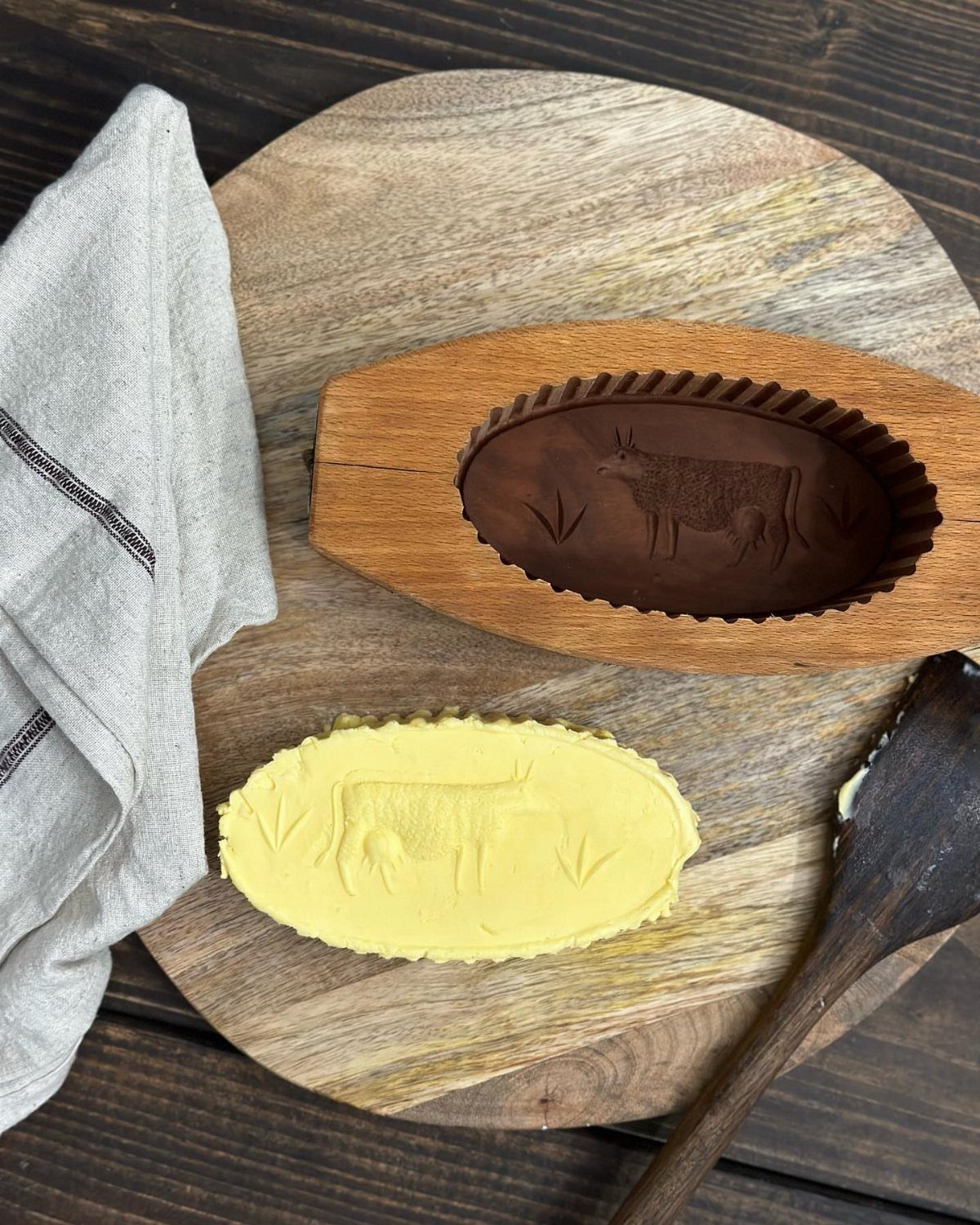 Wooden butter mold and cow-shaped butter on a round wooden cutting board.