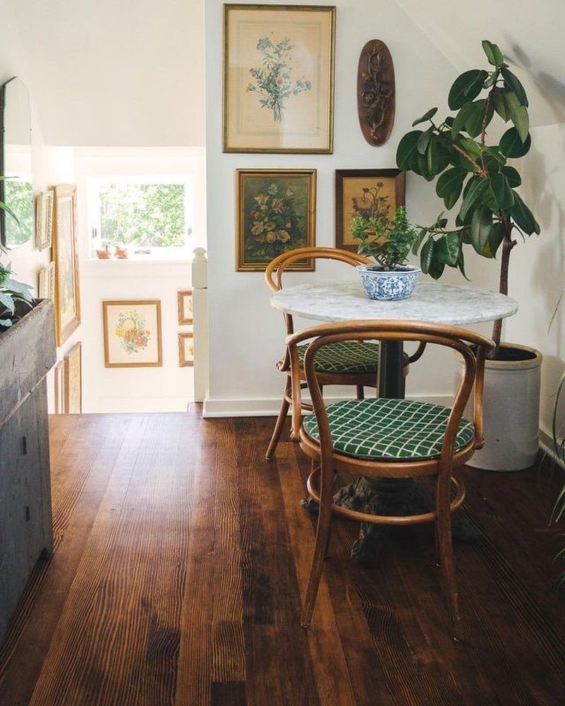 Round white marble café table with two wooden chairs on dark hardwood flooring.