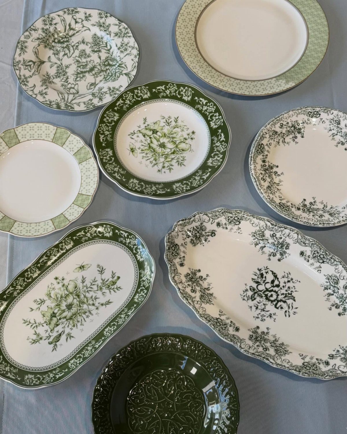 Vintage Plate Set Ideas: 12 Timeless Styles for Your Table 11 Green and white patterned ceramic plates and platters on a light blue tablecloth.