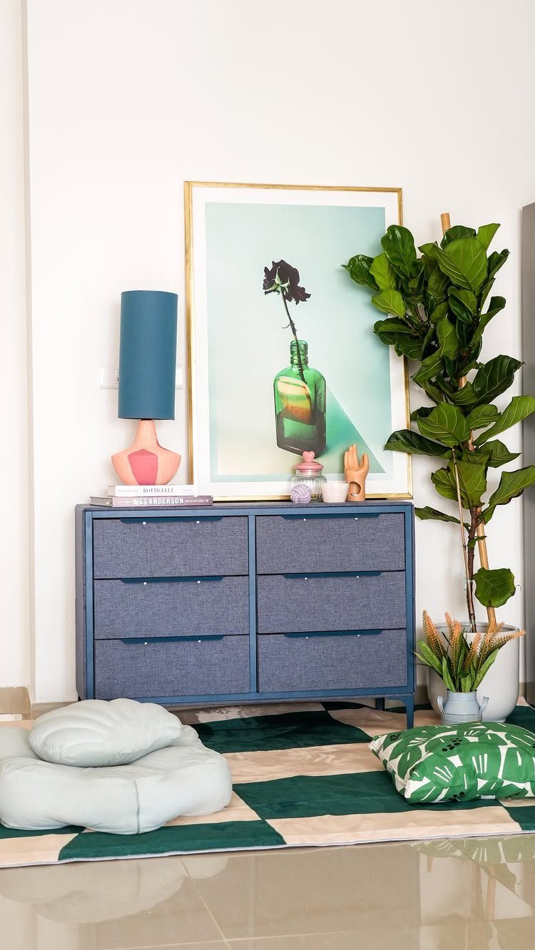 Blue fabric dresser with closed drawers, a lamp, and a large potted plant.