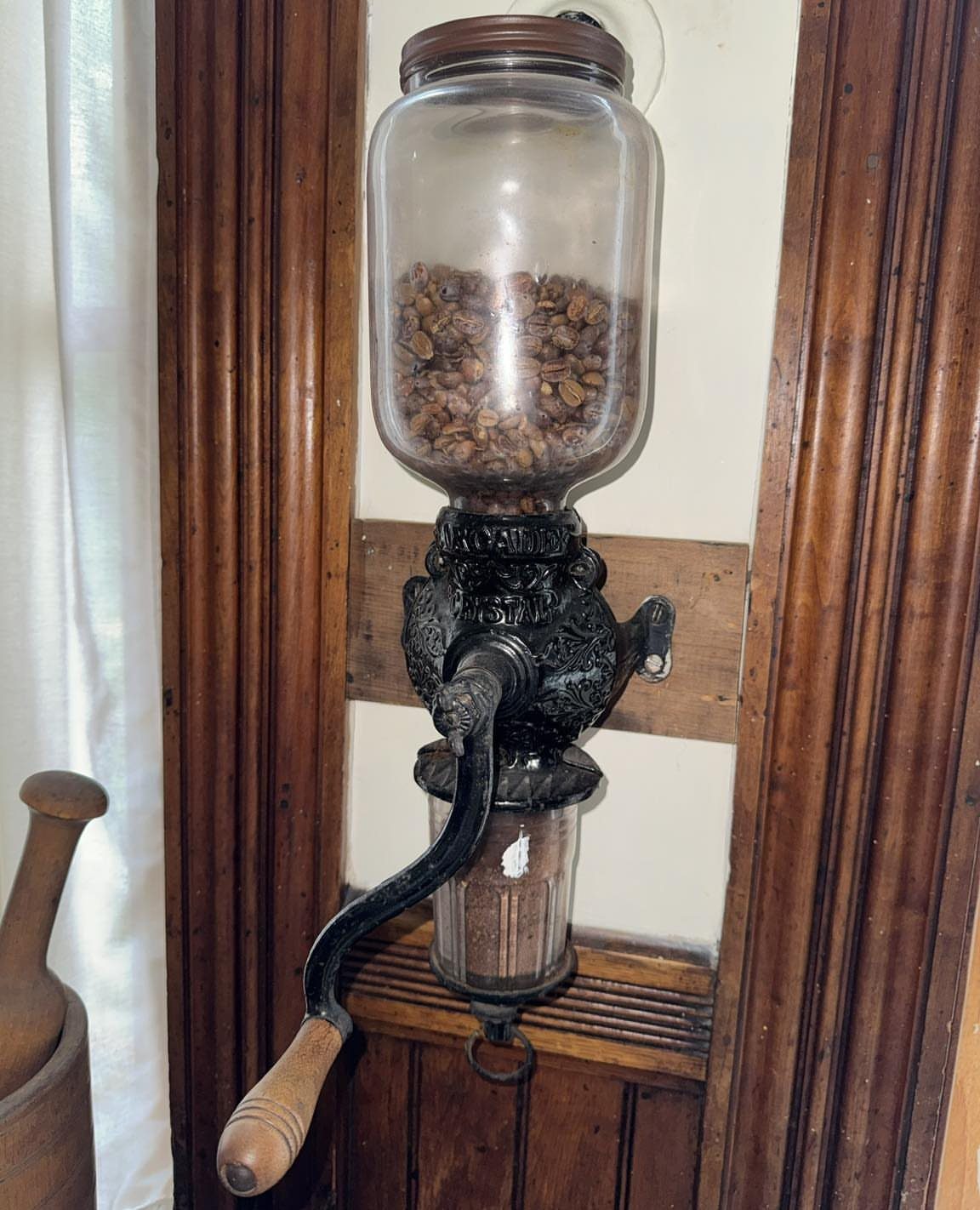 Vintage wall-mounted coffee grinder with glass bean hopper and hand crank on wooden wall
