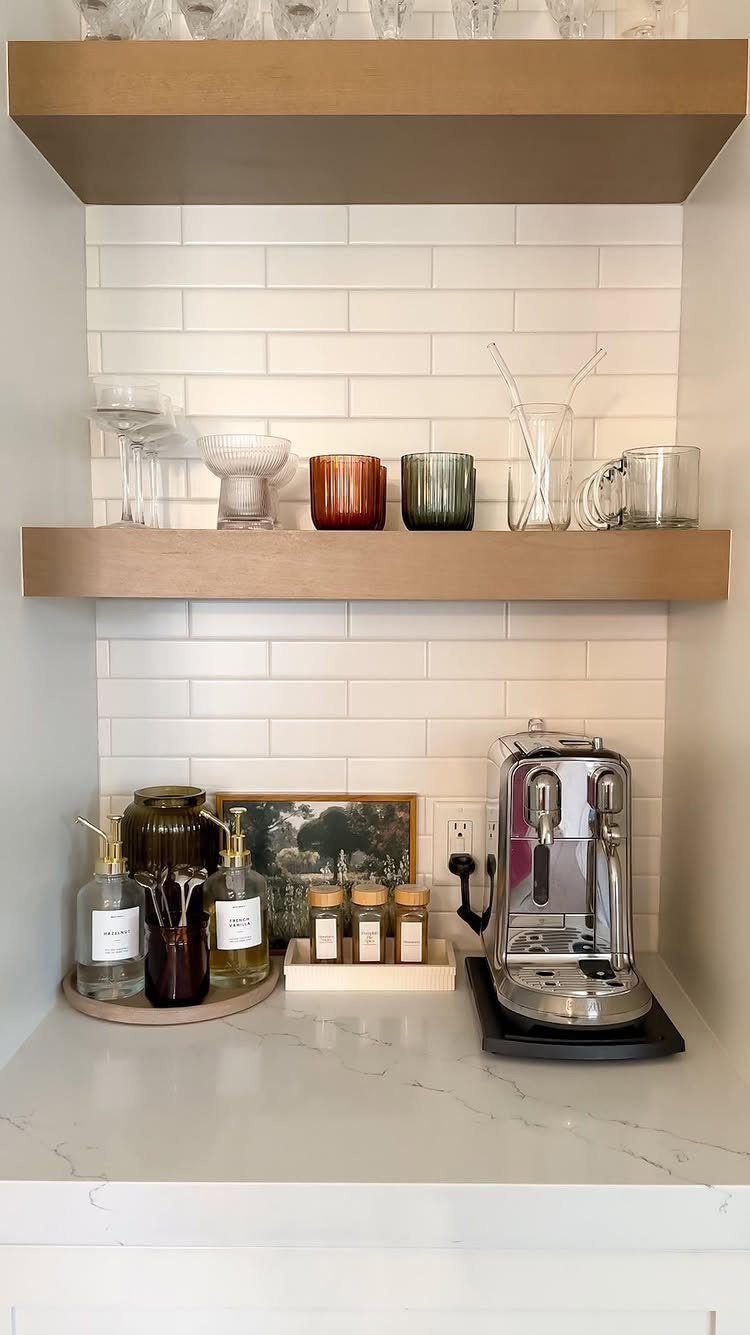 Coffee nook with silver espresso machine, syrup bottles, and wooden floating shelves.