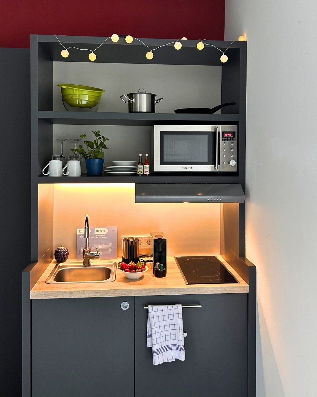 Compact dark grey kitchenette with small sink, induction hob, and microwave in small space.