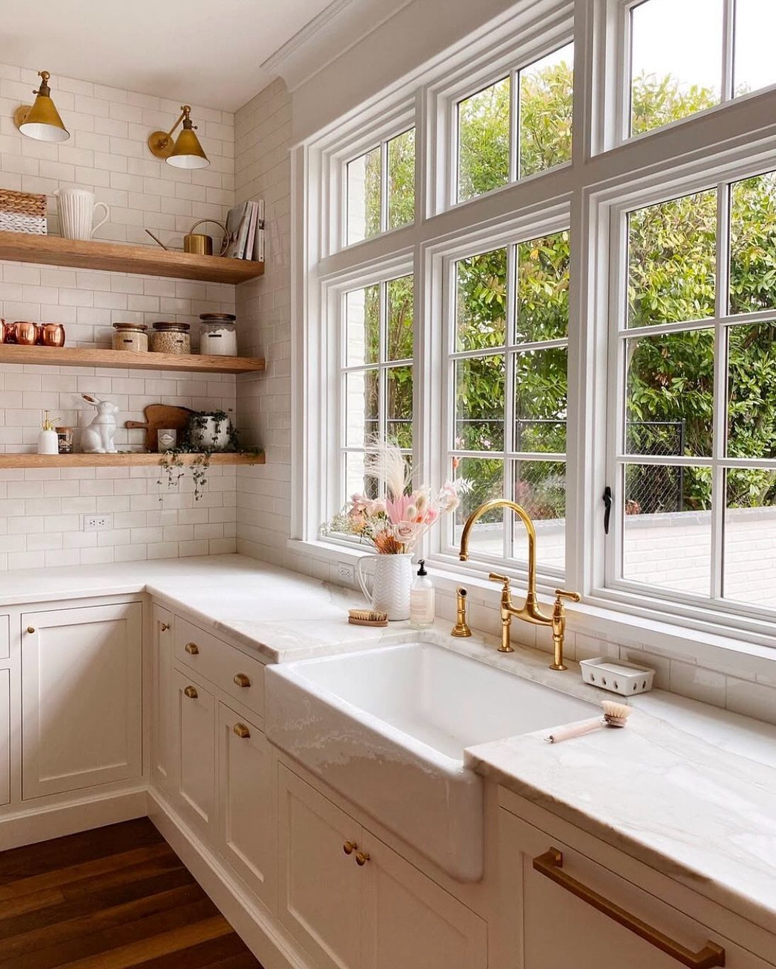 Small Kitchen Sink Ideas: 26 Ways to Maximize Space and Style 17 White apron-front farmhouse sink with gold faucet beneath a large window in a kitchen.