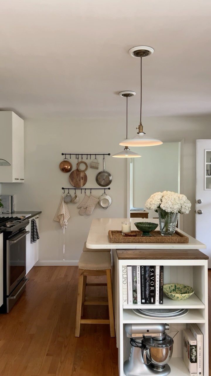 Small white kitchen with a central island, open shelving, and copper pots hanging.