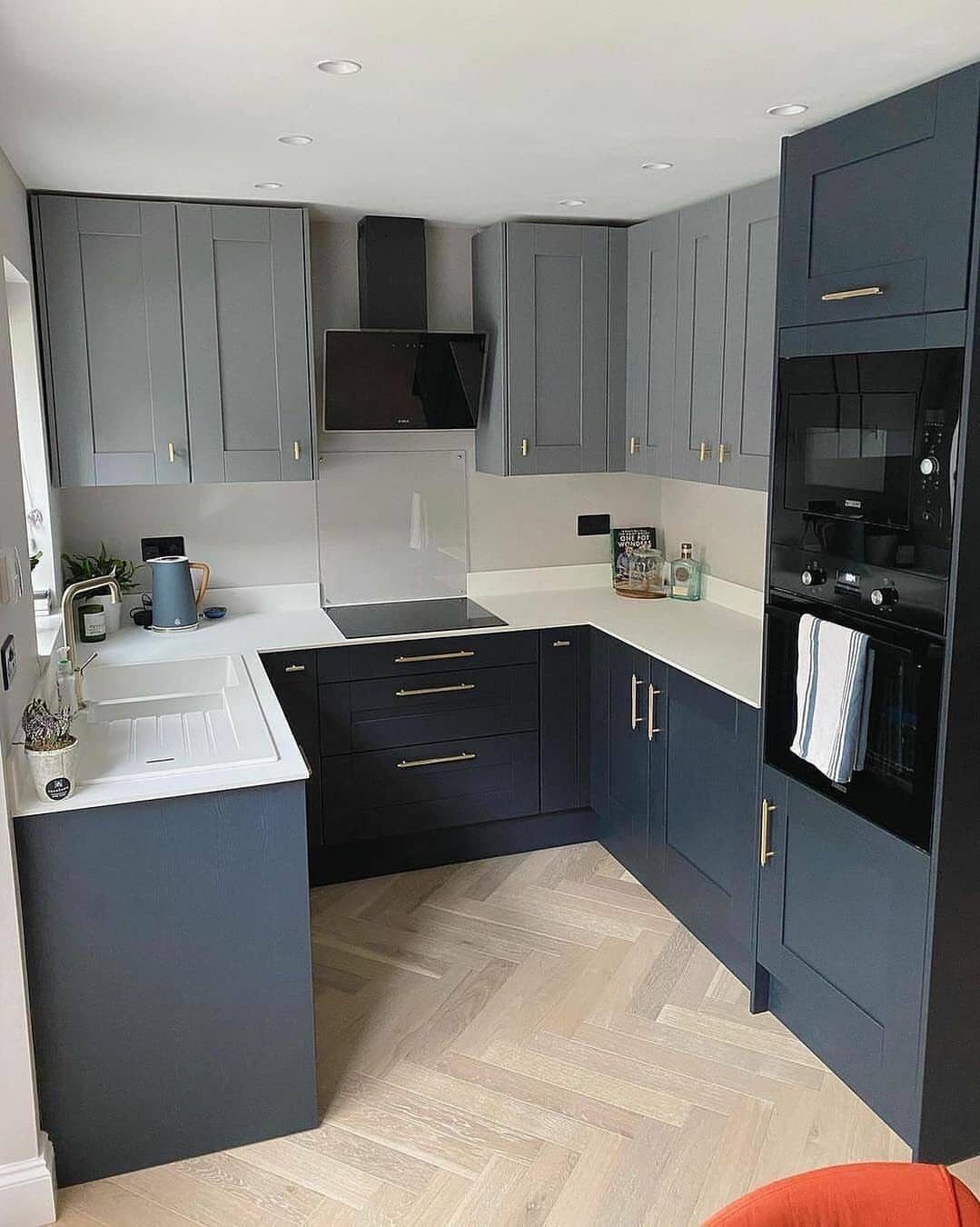 Small L-shaped kitchen with dark grey cabinets, white countertops, and herringbone wood floors.