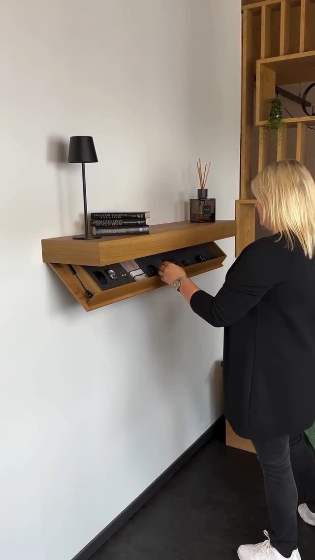 Wooden wall-mounted shelf with a flip-down panel concealing electronic equipment and knobs.
