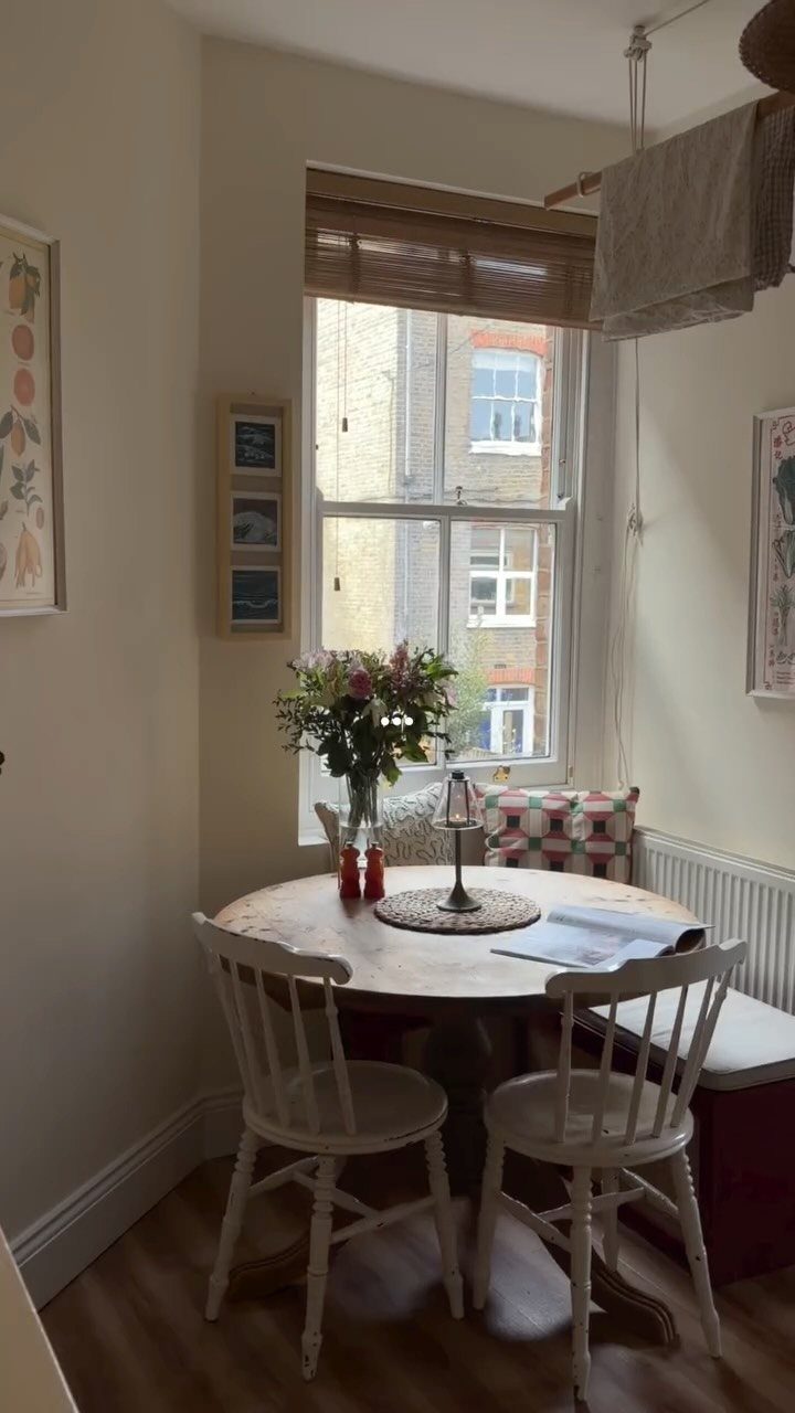 Round wooden dining table tucked into a corner with white chairs and bench seating.