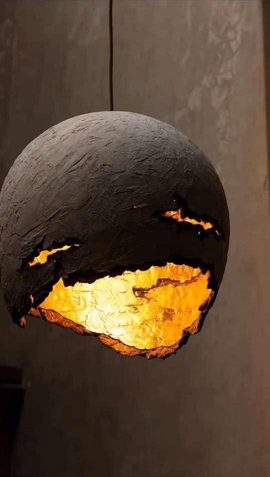 Spherical pendant light with a cracked dark shell and glowing golden interior.