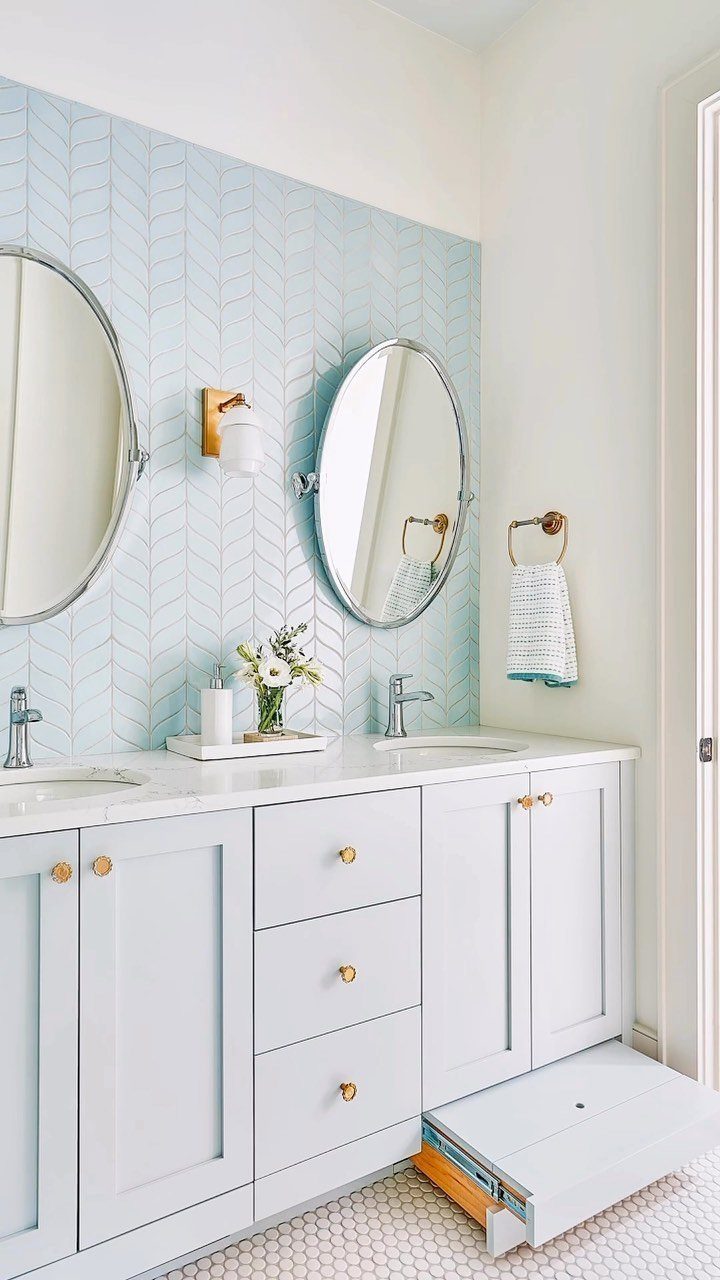 White double vanity with gold hardware and light blue herringbone tile backsplash.
