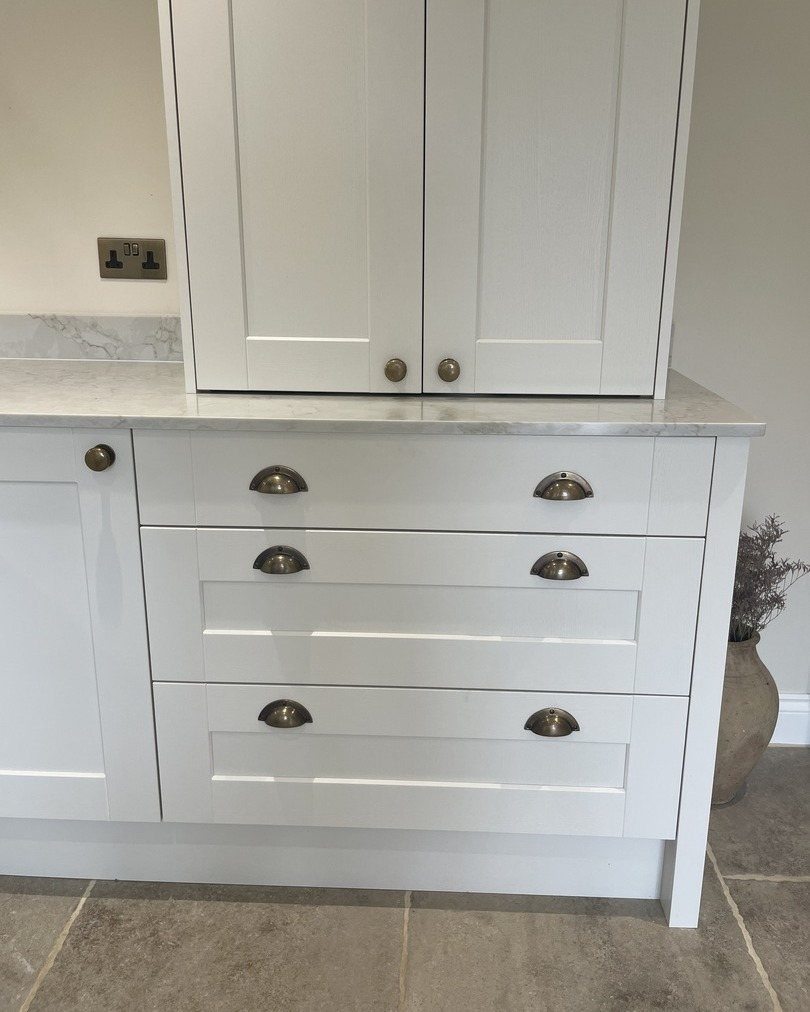 12 Kitchen Cabinet Handles Ideas to Refresh Your Space 3 White kitchen drawers with semi-circular metal cup pulls and round cabinet knobs.