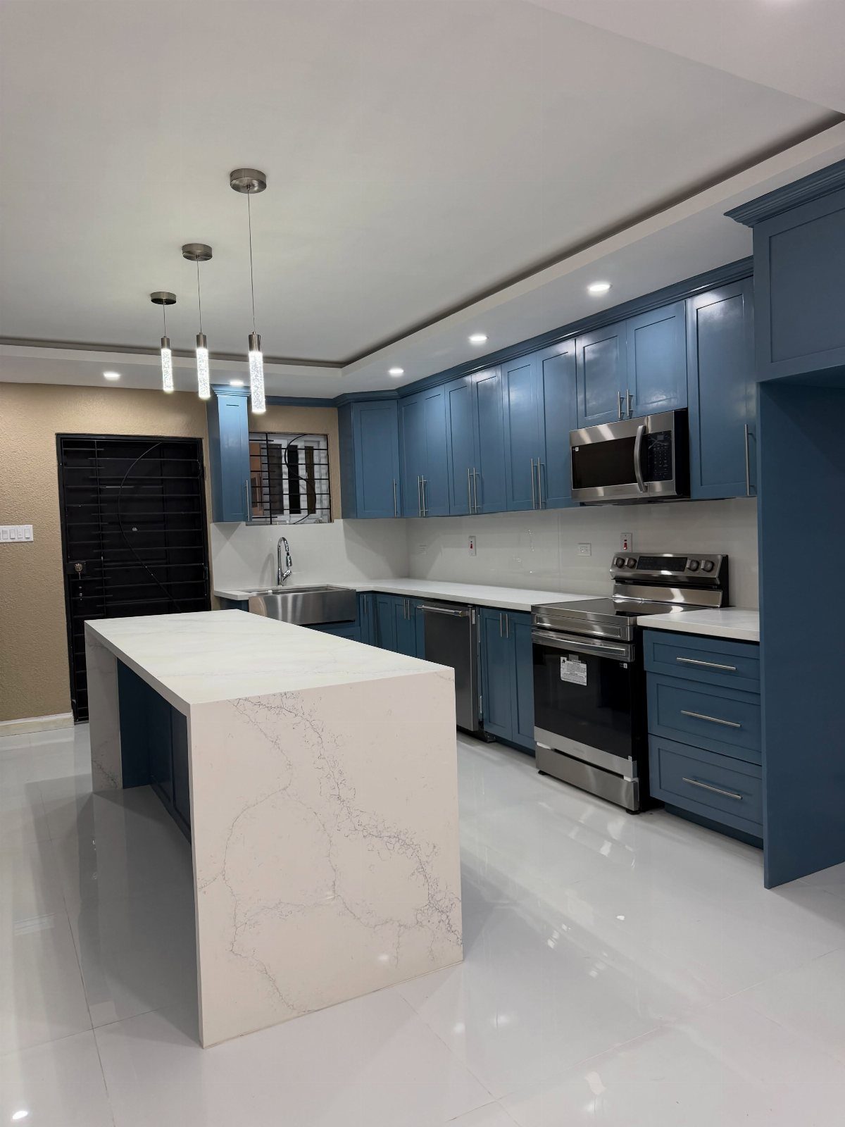 Blue kitchen cabinets with white countertops and a large white marble island.