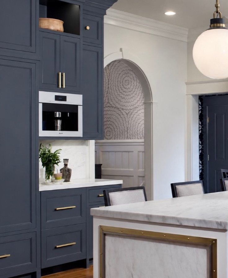 Dark blue kitchen cabinets with gold hardware and white marble countertops.