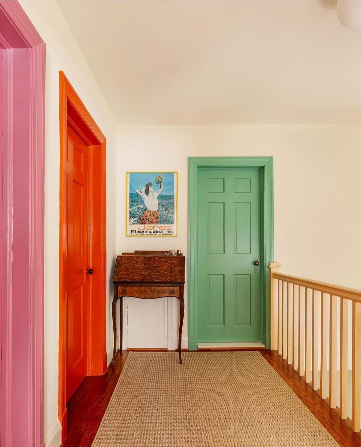 Colorful hallway with pink, orange, and green doors and a vintage wooden desk.