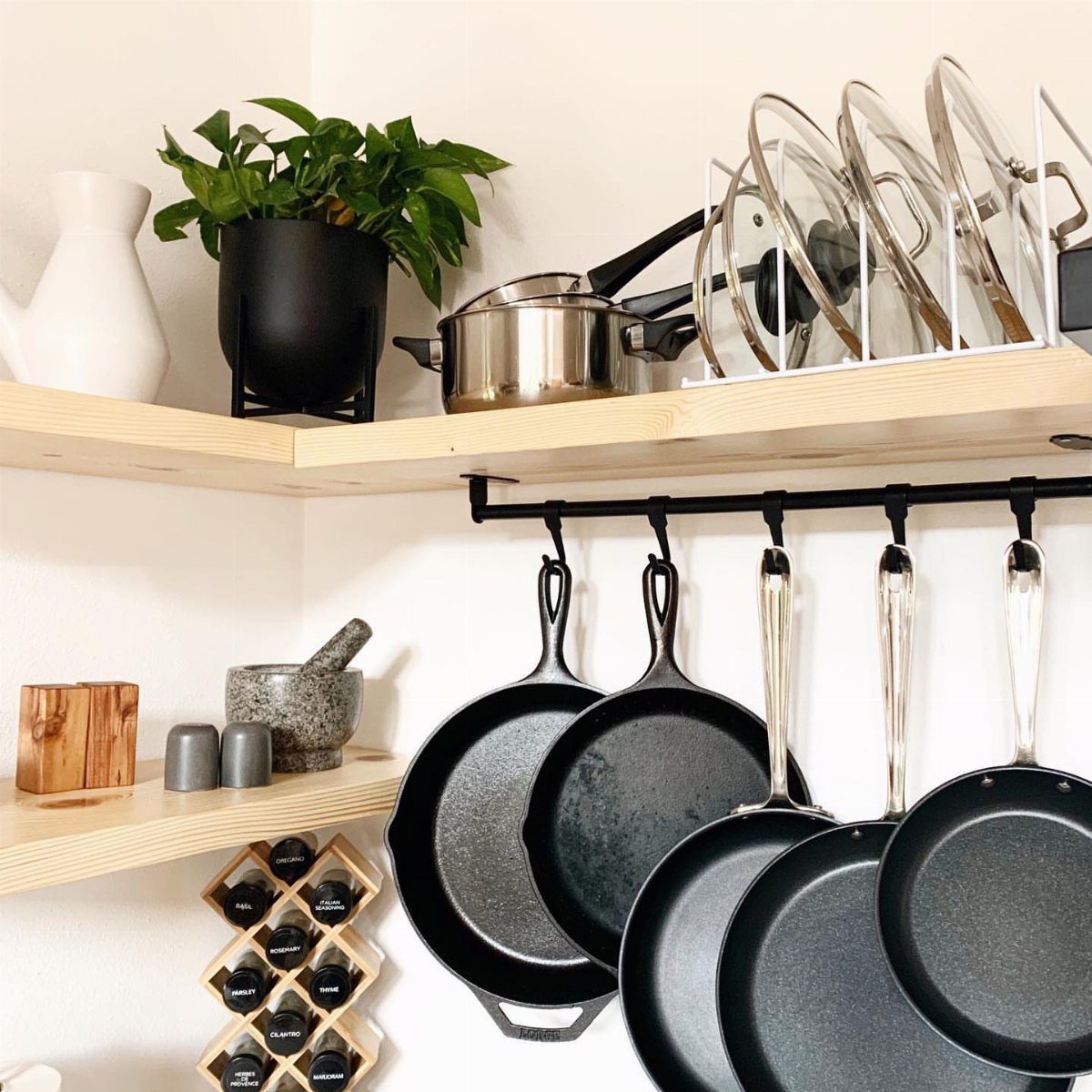 Wooden shelf with cookware hooks holding black frying pans and a lid organizer.