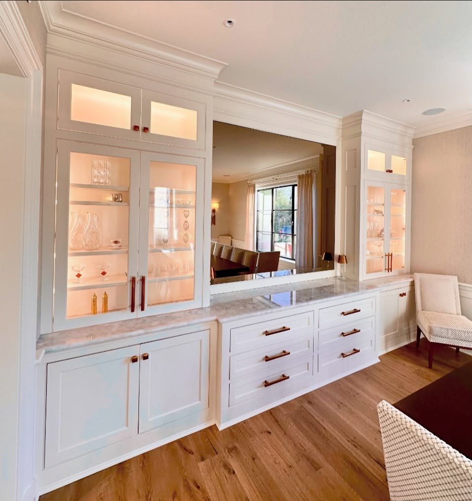 Dining Room Armoire: 16 Ideas for Storage and Style 17 White built-in dining cabinets with warm interior lighting illuminating glassware behind glass doors.