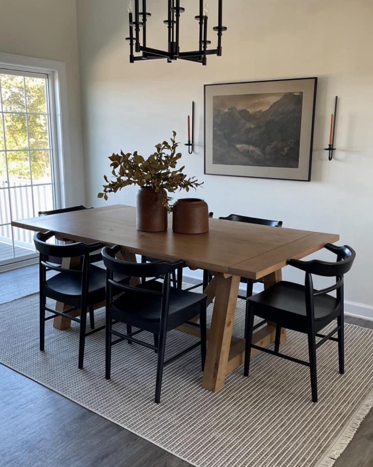 Wooden dining table and black chairs centered on a light textured area rug.