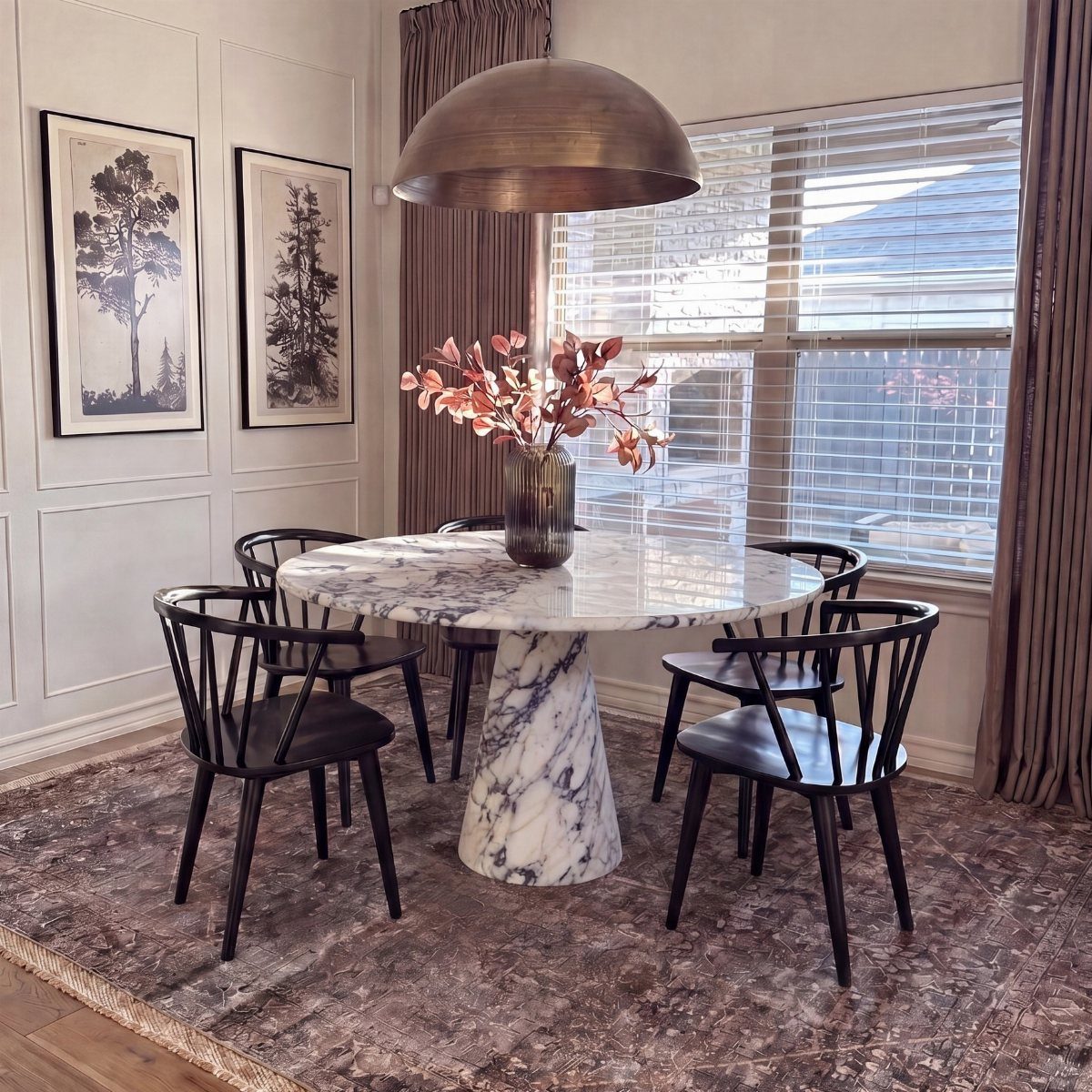Round white marble pedestal dining table with black chairs on a grey rug