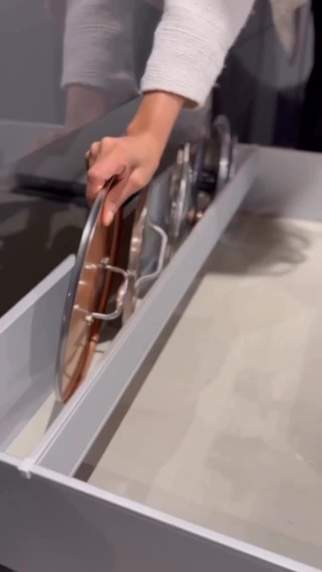 Glass pan lids stored vertically in a grey kitchen drawer divider rack