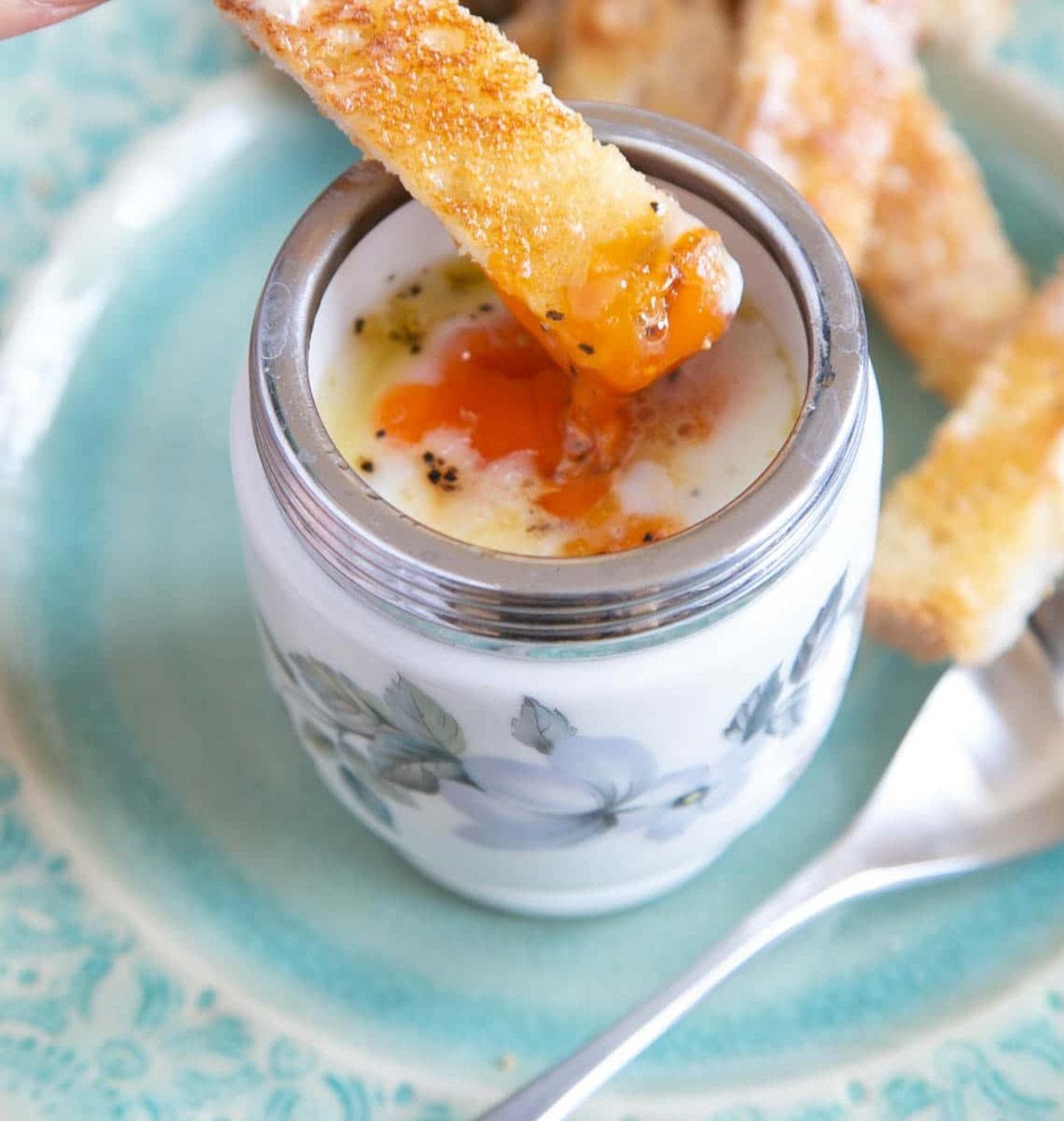 Egg coddler with a soft-cooked egg and toasted bread on a blue plate.