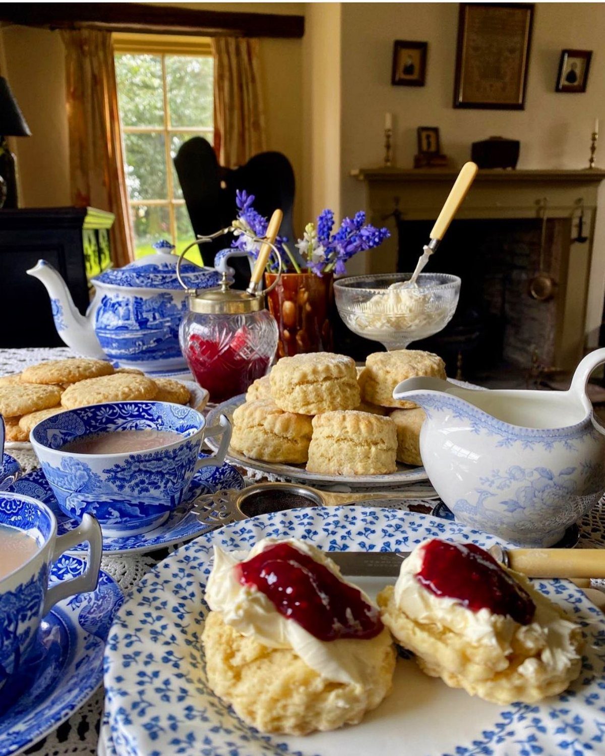 Blue and white floral porcelain tea set with scones, jam, and cream on a table.
