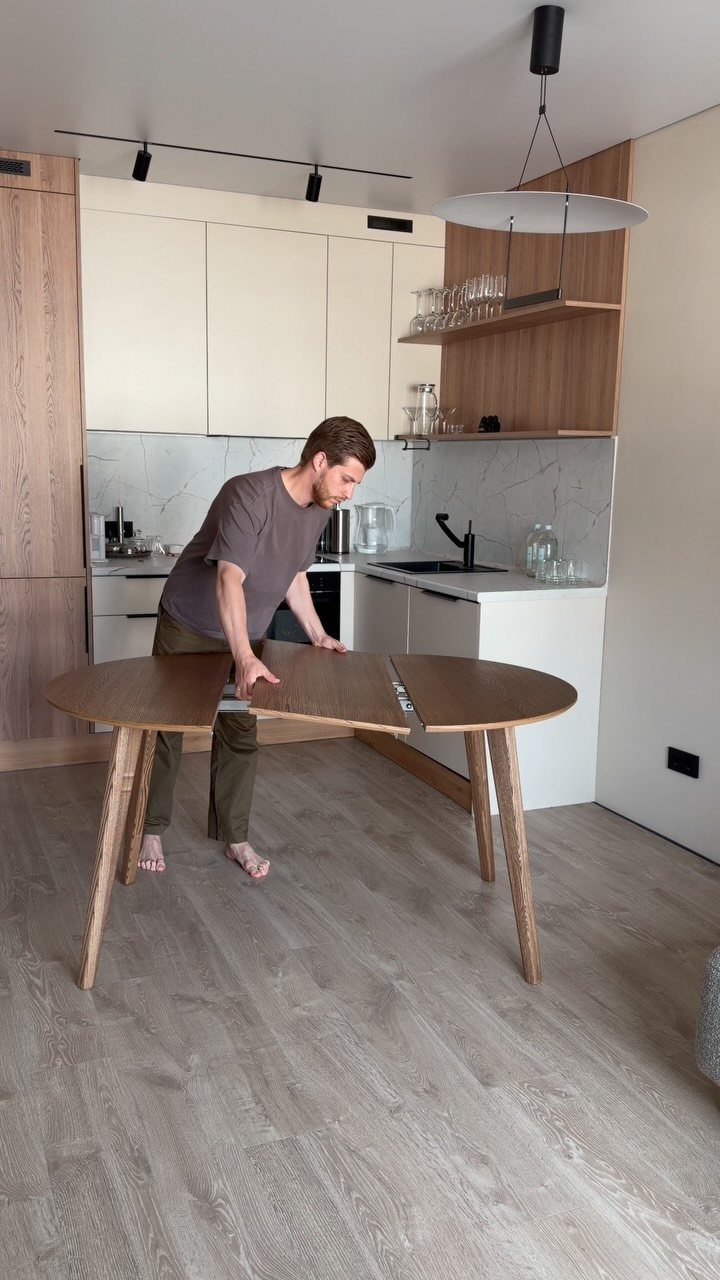 Man extending a wooden oval dining table in a modern white kitchen.