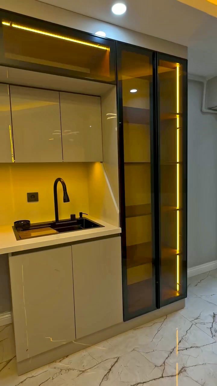 Modern kitchen with light cabinets and a tall black-framed glass cabinet with yellow lighting.