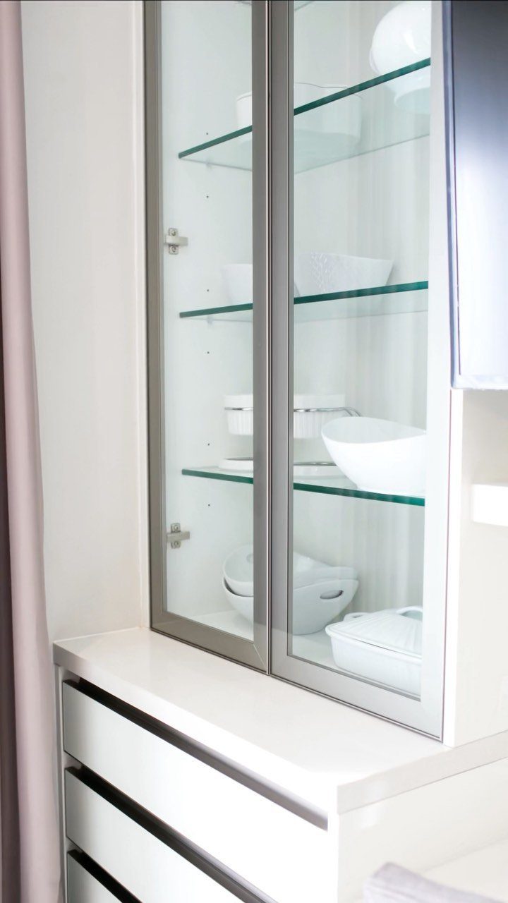 Glass-fronted kitchen cabinets with silver frames displaying white bowls on glass shelves.
