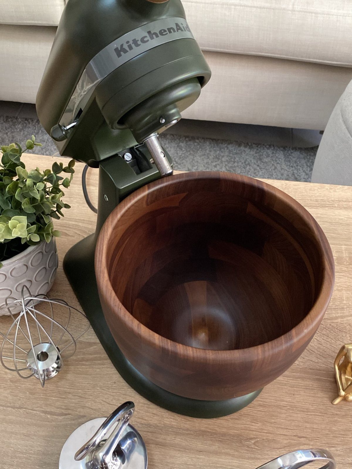 Green KitchenAid stand mixer with a polished wooden bowl on a wooden table.