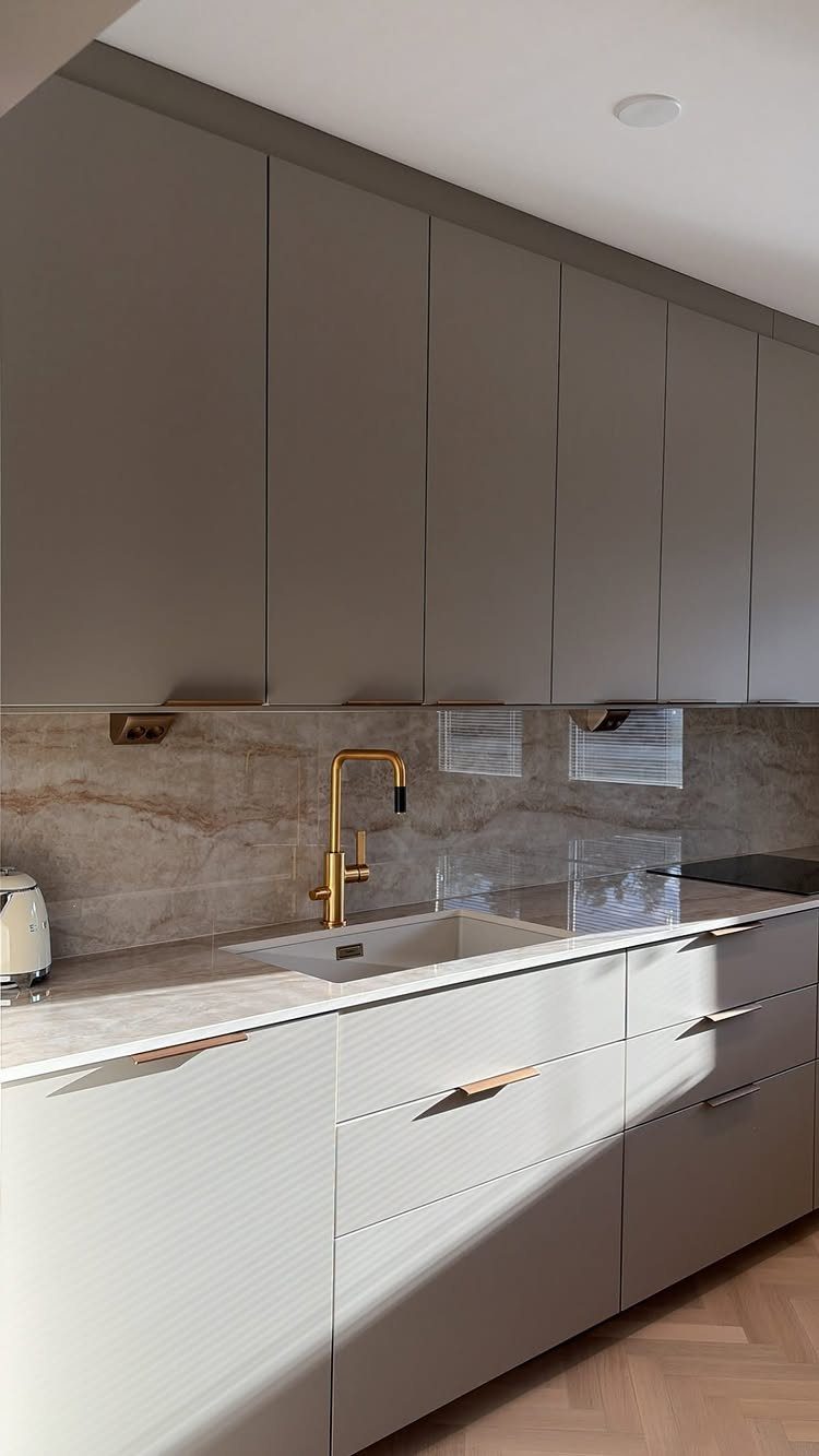 Grey kitchen cabinets featuring gold hardware, a gold faucet, and marble countertops.