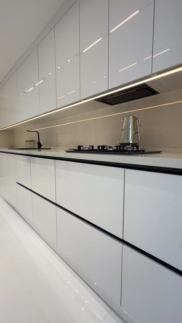 Glossy white handleless kitchen cabinets with a black countertop and integrated stovetop.