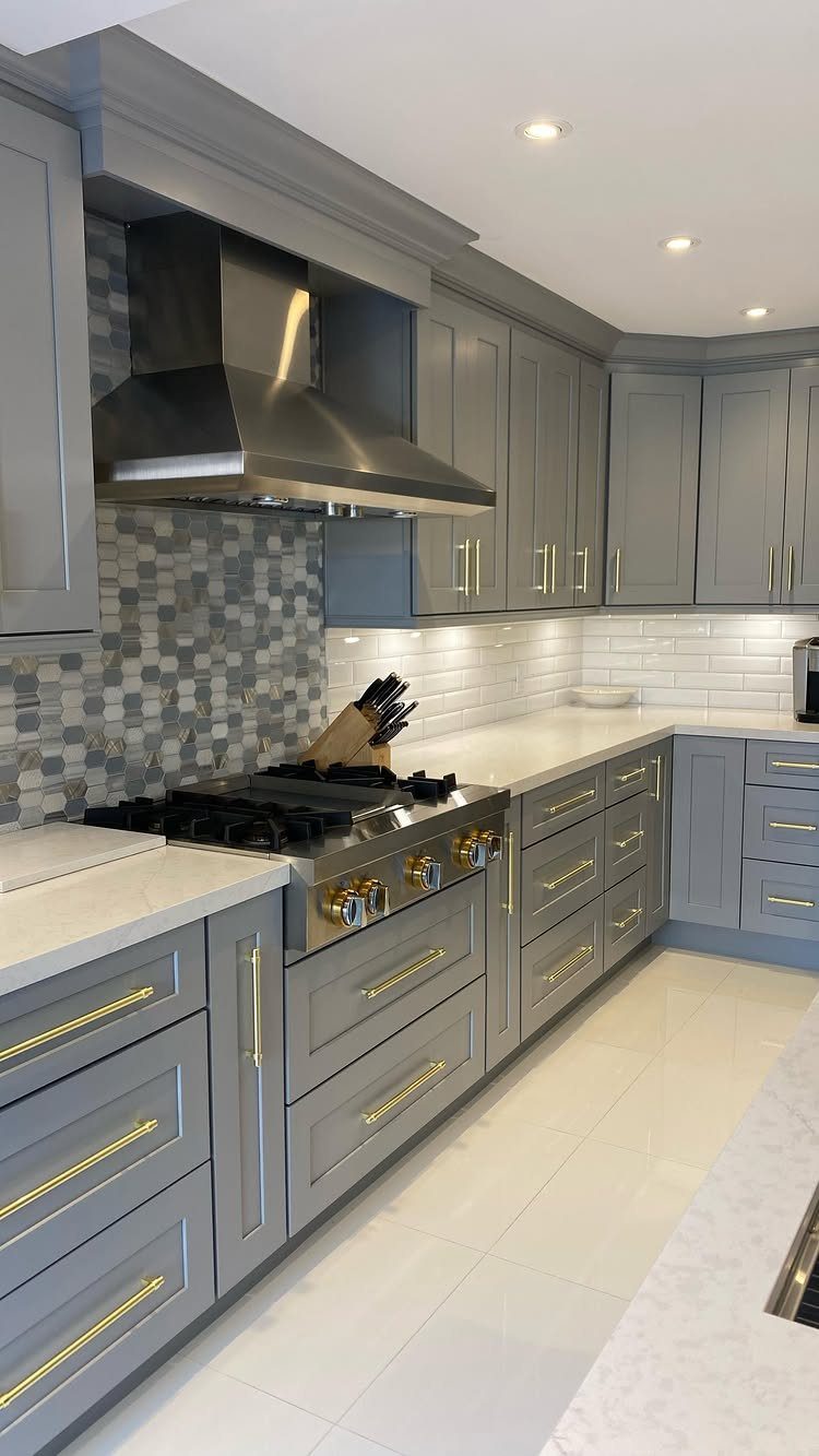 Grey kitchen cabinets with prominent gold hardware handles and a stainless steel range hood.