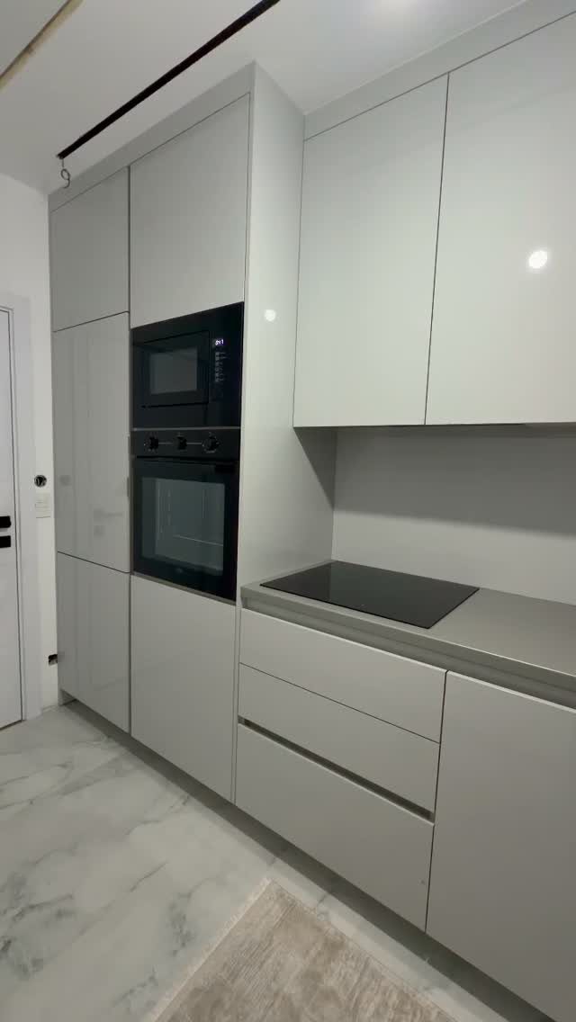 High-gloss white kitchen cabinets with integrated oven, microwave, and grey countertop.