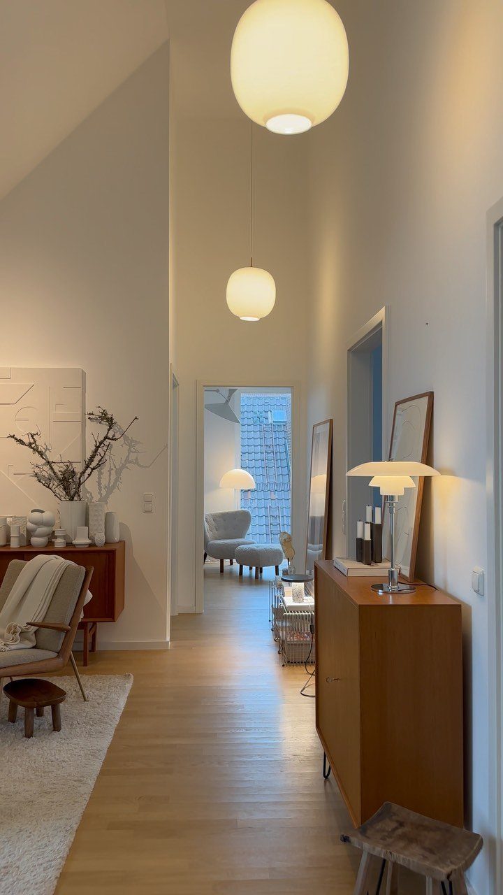 Minimalist living space with light wood floors, white walls, and spherical pendant lighting.