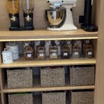 Light wood kitchen pantry shelves with a stand mixer, cereal dispensers, and wicker baskets.