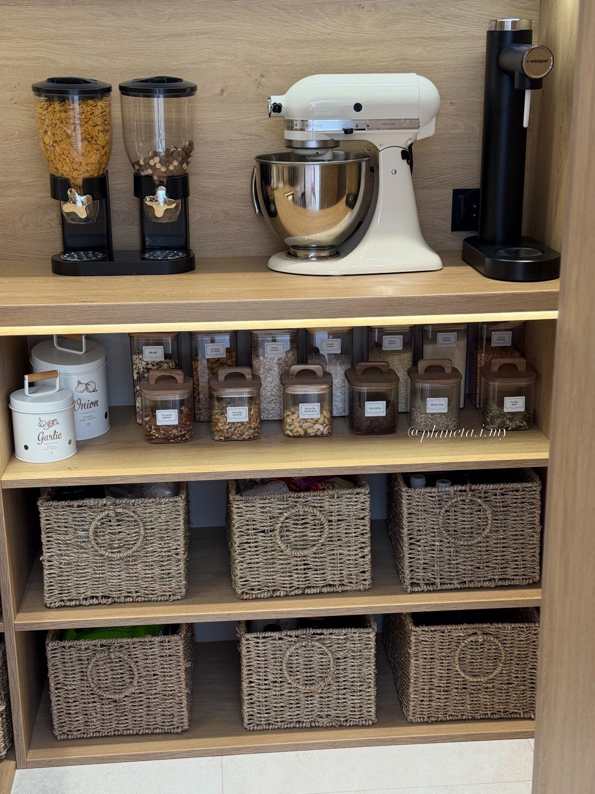 Light wood kitchen pantry shelves with a stand mixer, cereal dispensers, and wicker baskets.