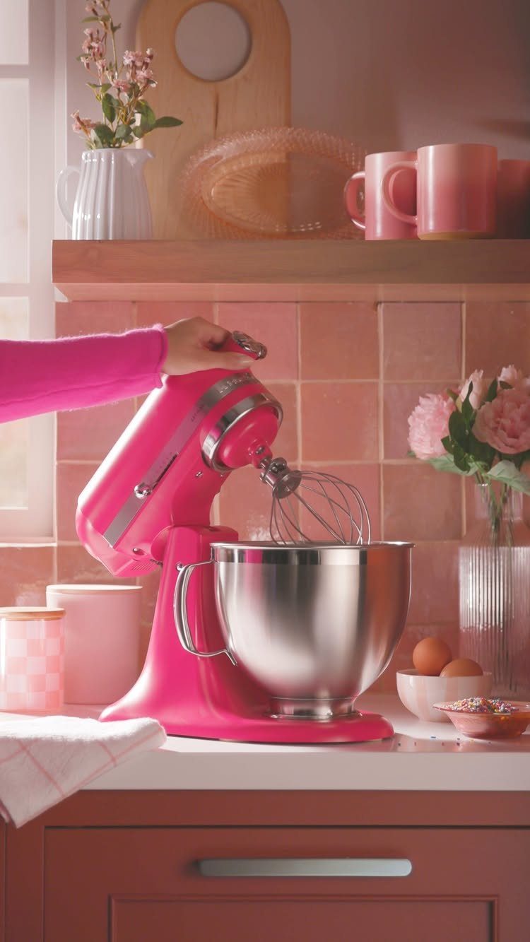Pink KitchenAid stand mixer with metal bowl on a white kitchen countertop.