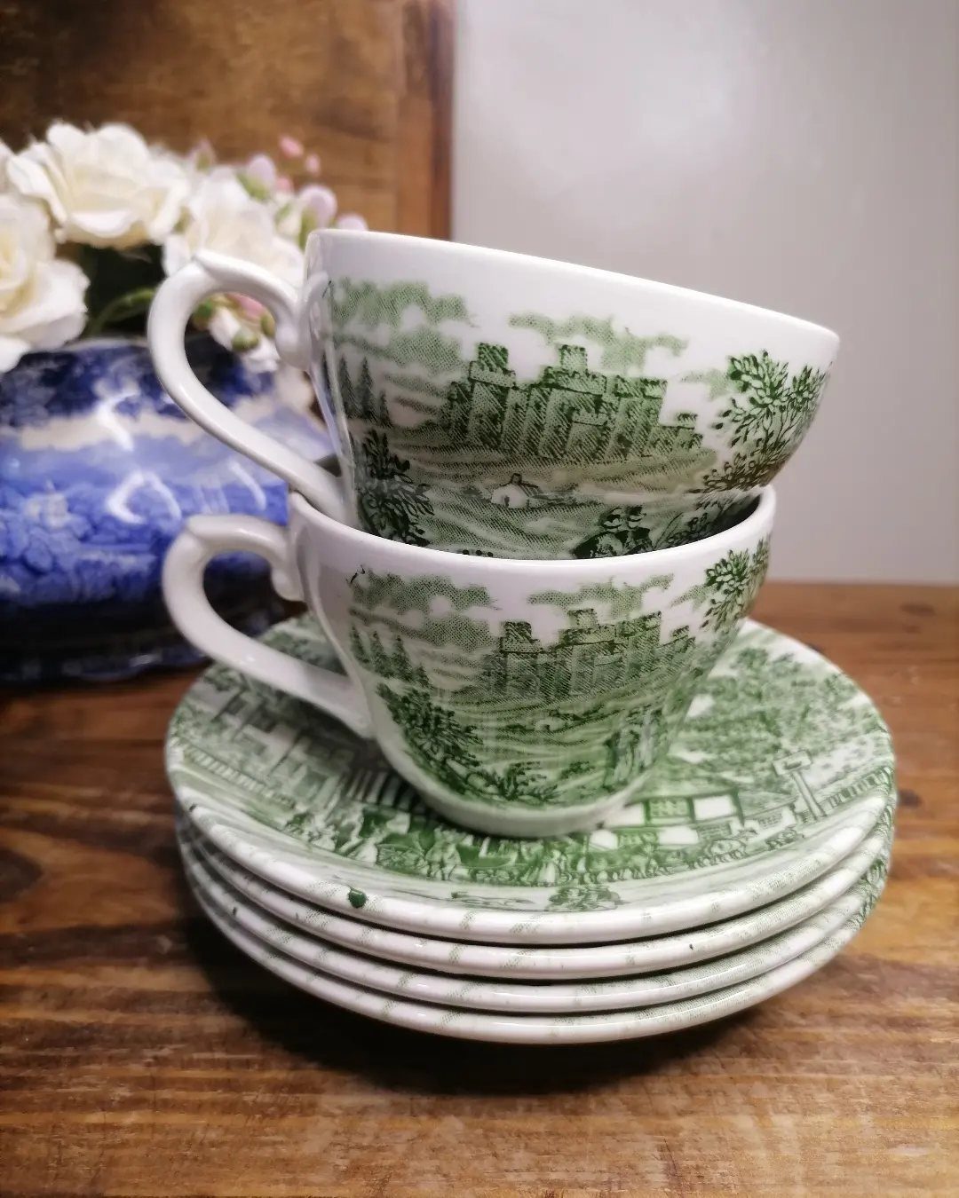 Vintage green and white ceramic teacups and saucers with castle illustrations on wood.