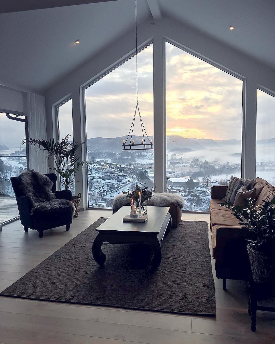 Modern living room with large glass windows overlooking a snowy mountain landscape at sunset.