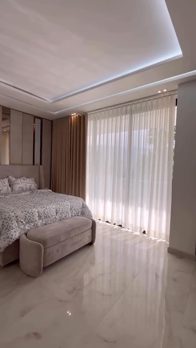 Large window with white sheer curtains in a modern, neutral toned bedroom