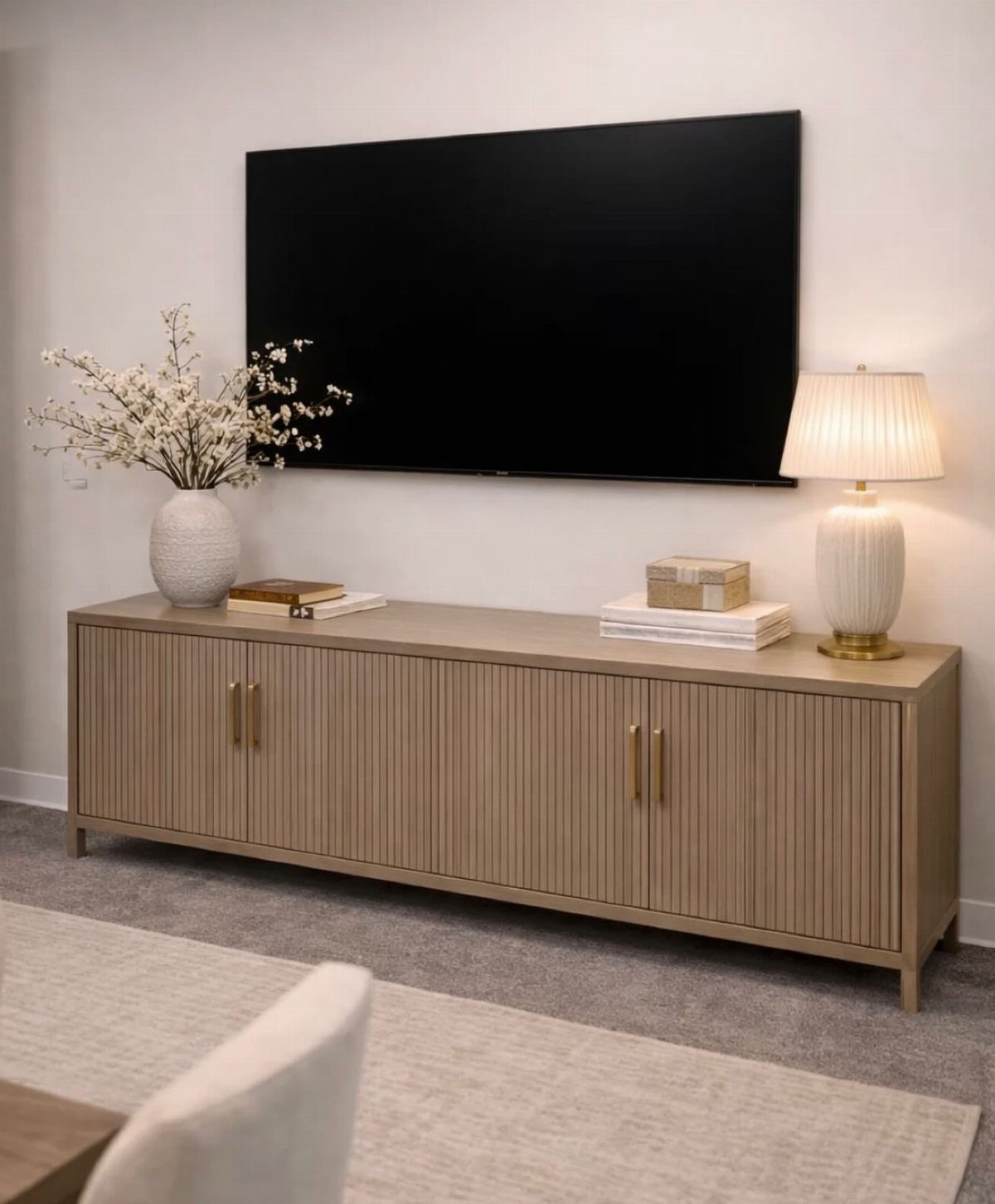 Light brown wooden media console with ribbed doors under a wall-mounted television.