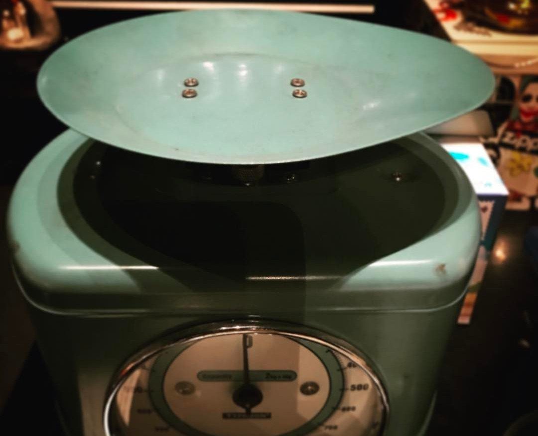 Vintage light blue-green manual kitchen scale with a circular weighing platform and analog dial.